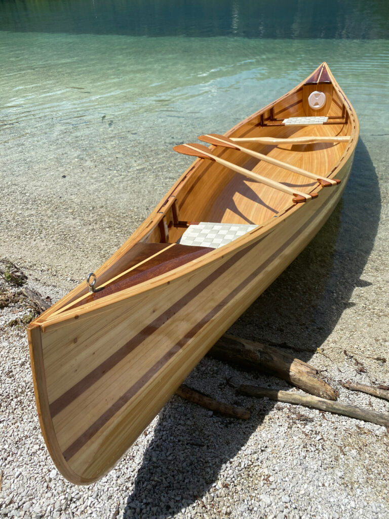 Innenansicht des Holzkanus am Ufer mit zwei bespannten Sitzen und zwei Holzpaddeln.