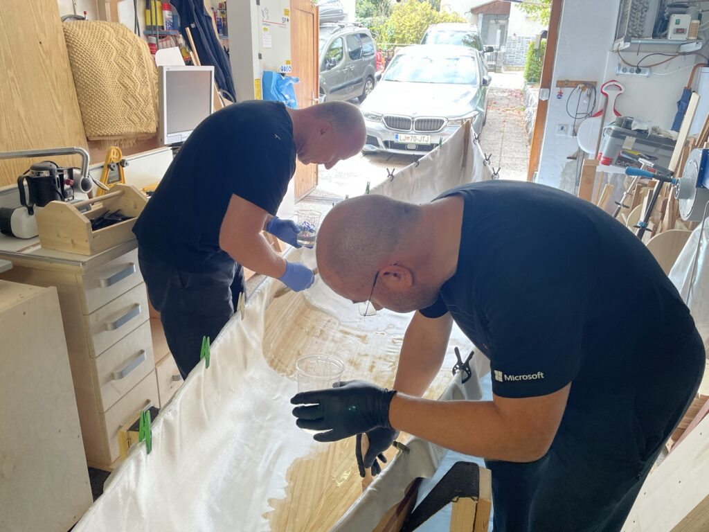 Zwei Personen verarbeiten Glasgewebe am Kanurumpf in der Werkstatt.