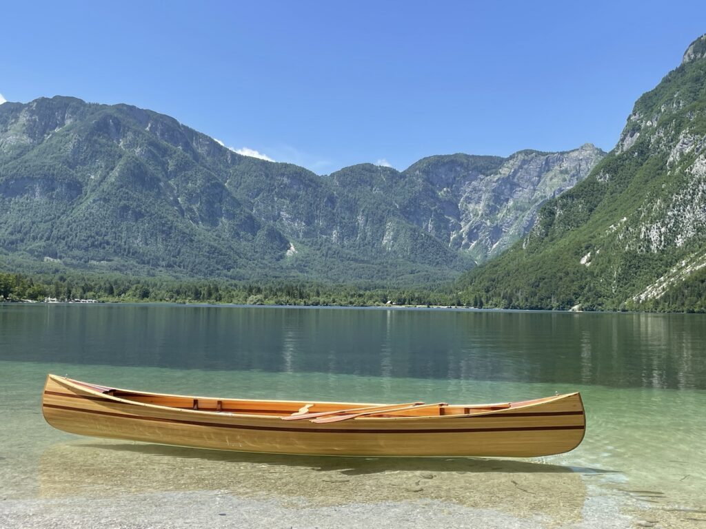 Seitenansicht des fertigen Holzkanus im flachen, klaren Wasser vor einer Bergkulisse.